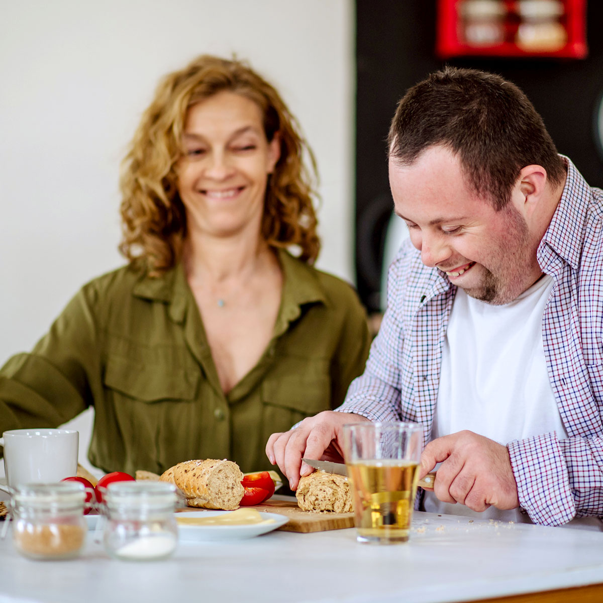Portrait of happy young man with Down syndrome with his carer at home having breakfast together.