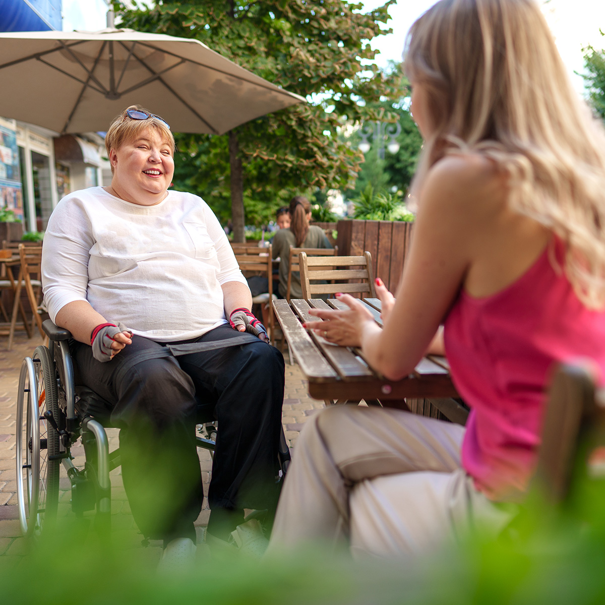 Mother with disability in wheelchair talking to her daughter while sitting at the table in cafe
