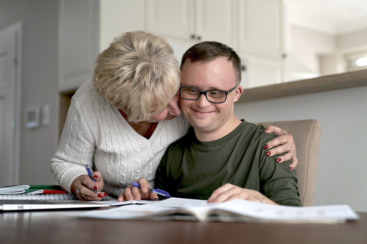 Mother hugging caucasian man with down syndrome while learning at home