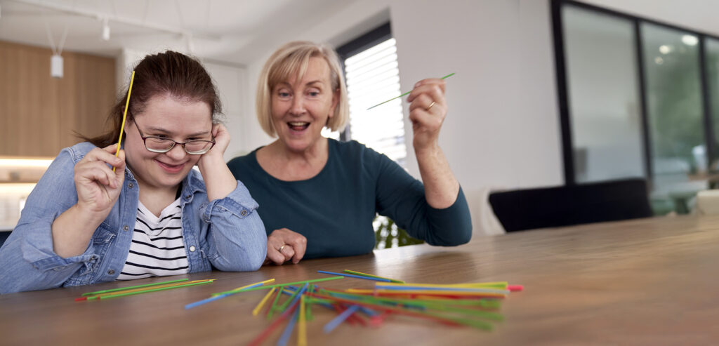 Down syndrome woman and her carer playing pick up sticks at home